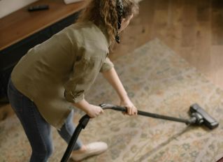 High-angle view of a woman vacuuming a patterned carpet in a stylish living room.
